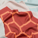 Babydecke in naturweiss orange rot und weich in mehrfarbigem grafischem Muster aus Merinowolle und Mohair für zeitloses Baby Interieur in frischem Design mit Nachhaltigkeit als das perfekte Geschenk für Neugeborene im Babybett