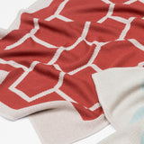 Babydecke in naturweiss rot und weich in mehrfarbigem grafischem Muster aus Merinowolle und Mohair für zeitloses Baby Interieur in frischem Design mit Nachhaltigkeit als das perfekte Geschenk für Neugeborene im Babybett