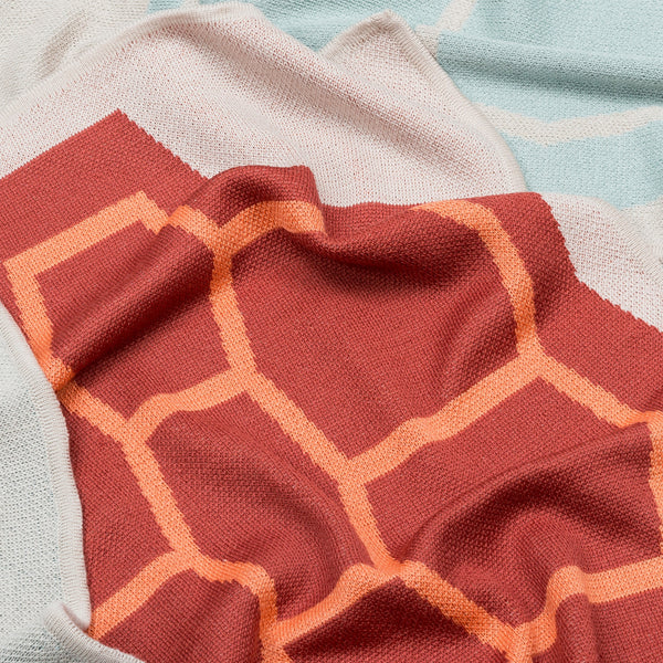 Babydecke in naturweiss orange rot und weich in mehrfarbigem grafischem Muster aus Merinowolle und Mohair für zeitloses Baby Interieur in frischem Design mit Nachhaltigkeit als das perfekte Geschenk für Neugeborene im Babybett