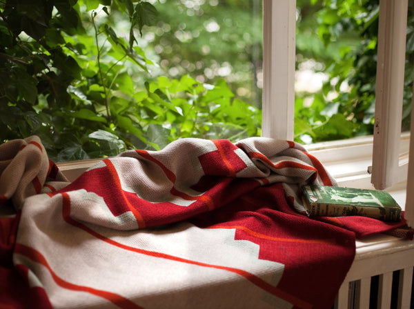 Wolldecke in rot und naturweiss mit buntem grafischen Muster aus Merino und Mohair gestrickt als zeitloses Plaid Interieur-Accessoire für Zuhause in luxuriösem Design mit Nachhaltigkeit und das perfekte Geschenk für jedes Sofa und vor Kamin im Chalet